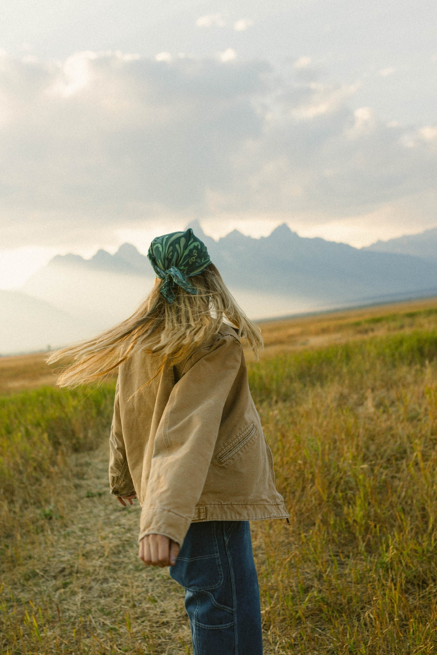 Woman wearing Sloan cotton bandana in aqua, enjoying the outdoors with mountains in the background.