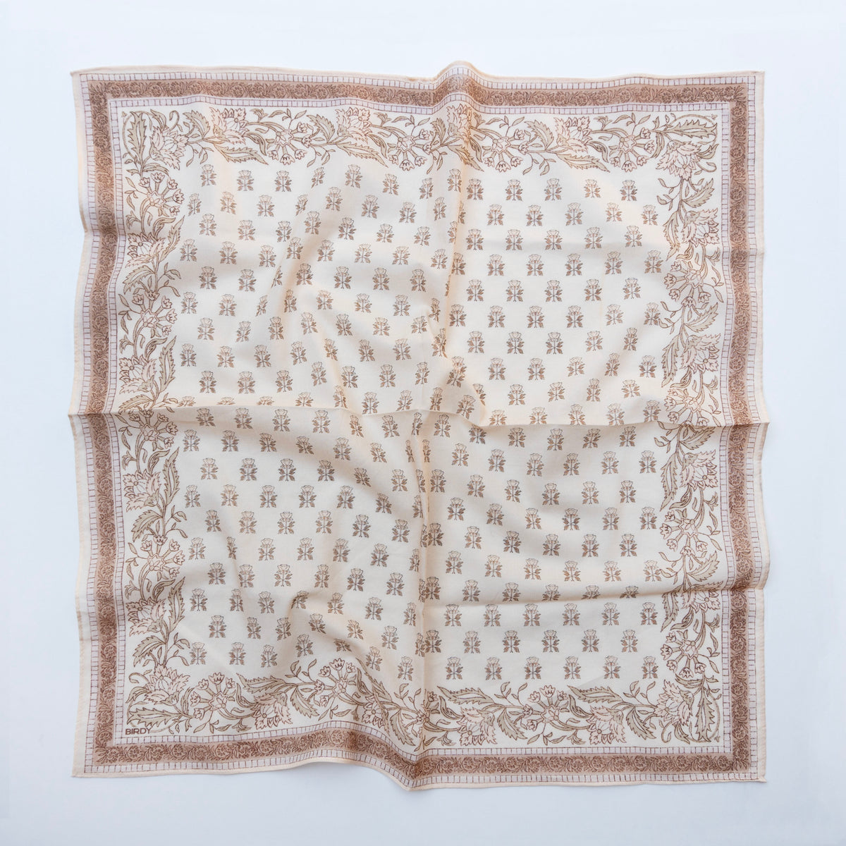 A square scarf laid flat on a light gray background, featuring a beige and brown botanical border with a repeating monogram pattern in the center.