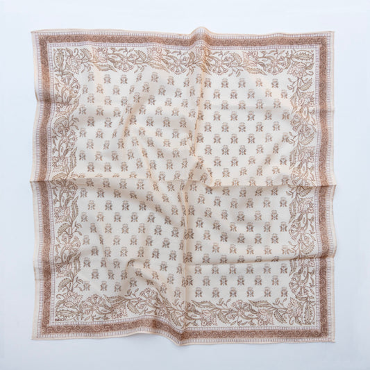 A square scarf laid flat on a light gray background, featuring a beige and brown botanical border with a repeating monogram pattern in the center.