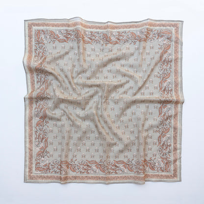 A square silk scarf with an intricate pattern of small monogram motifs and a floral border, laid flat on a white background.