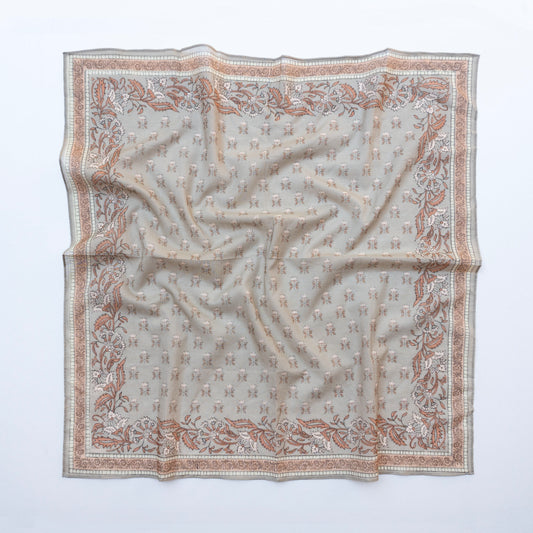 A square silk scarf with an intricate pattern of small monogram motifs and a floral border, laid flat on a white background.