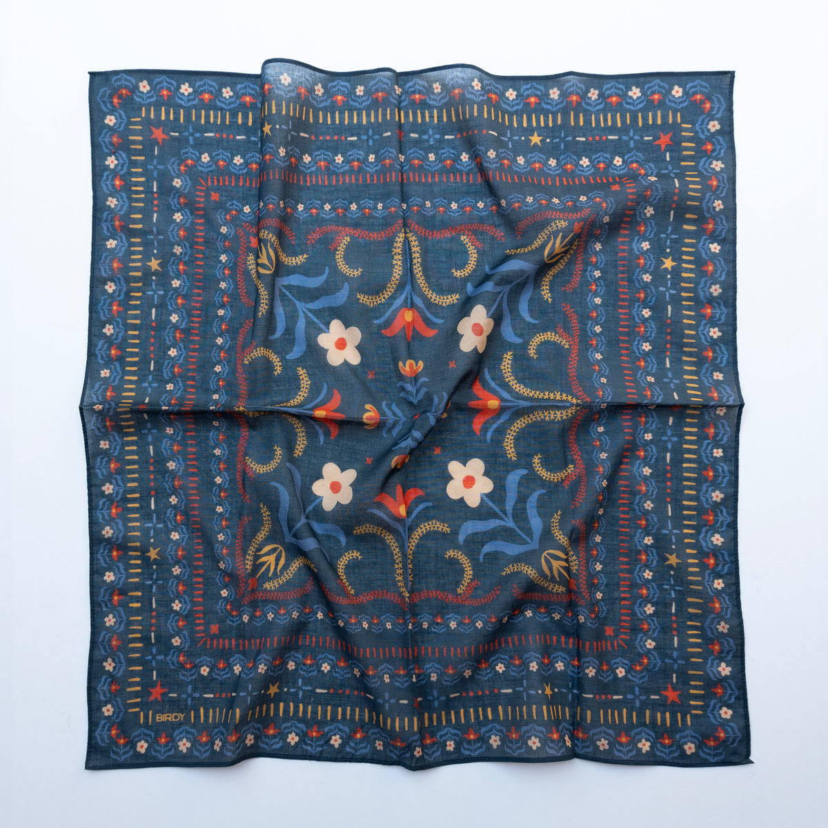 A square scarf with a dark navy blue base, featuring a detailed folk-art style border and central floral pattern in red, yellow, and white, laid flat on a white background.