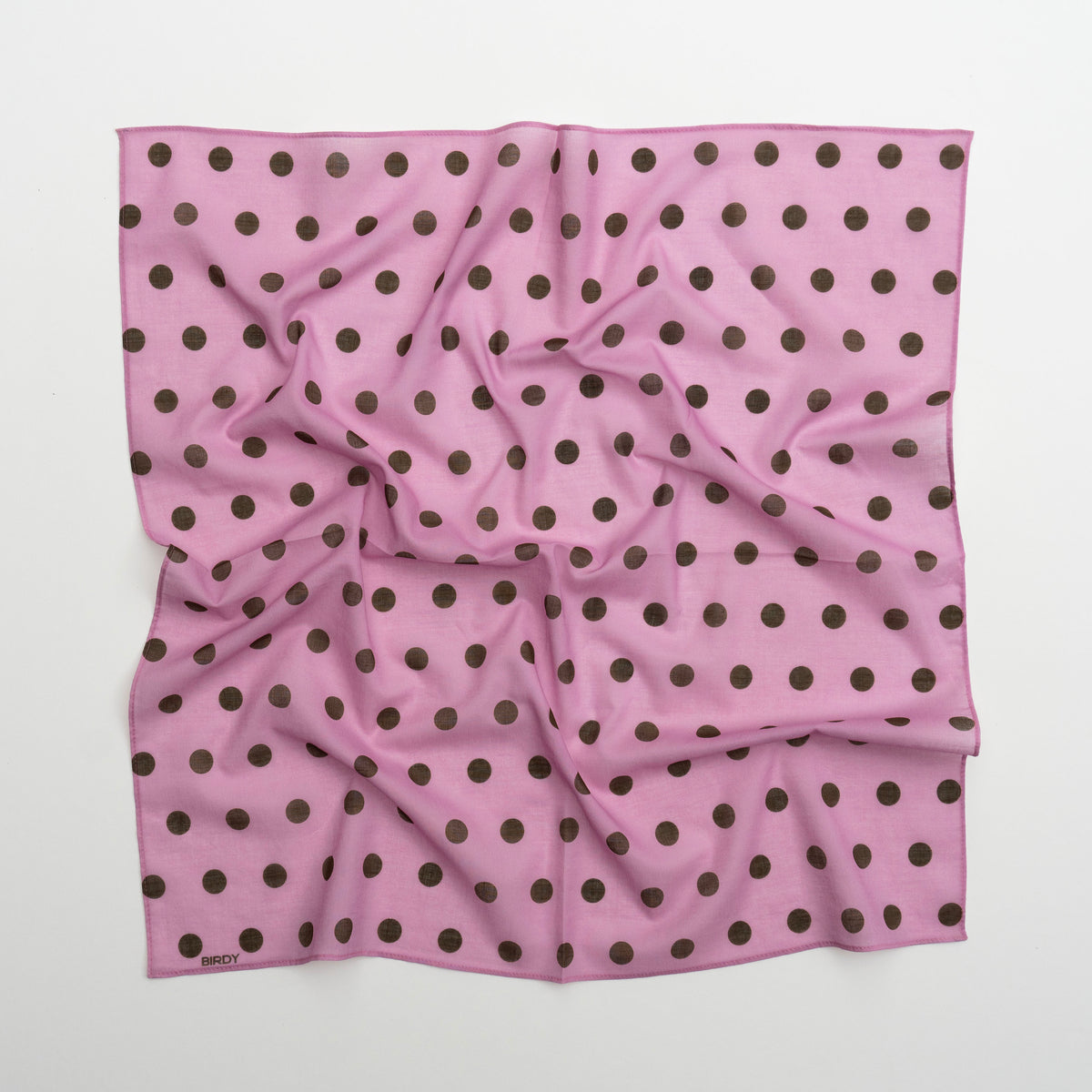 A square pink scarf with a repeating pattern of dark brown polka dots, laid flat on a light gray background.