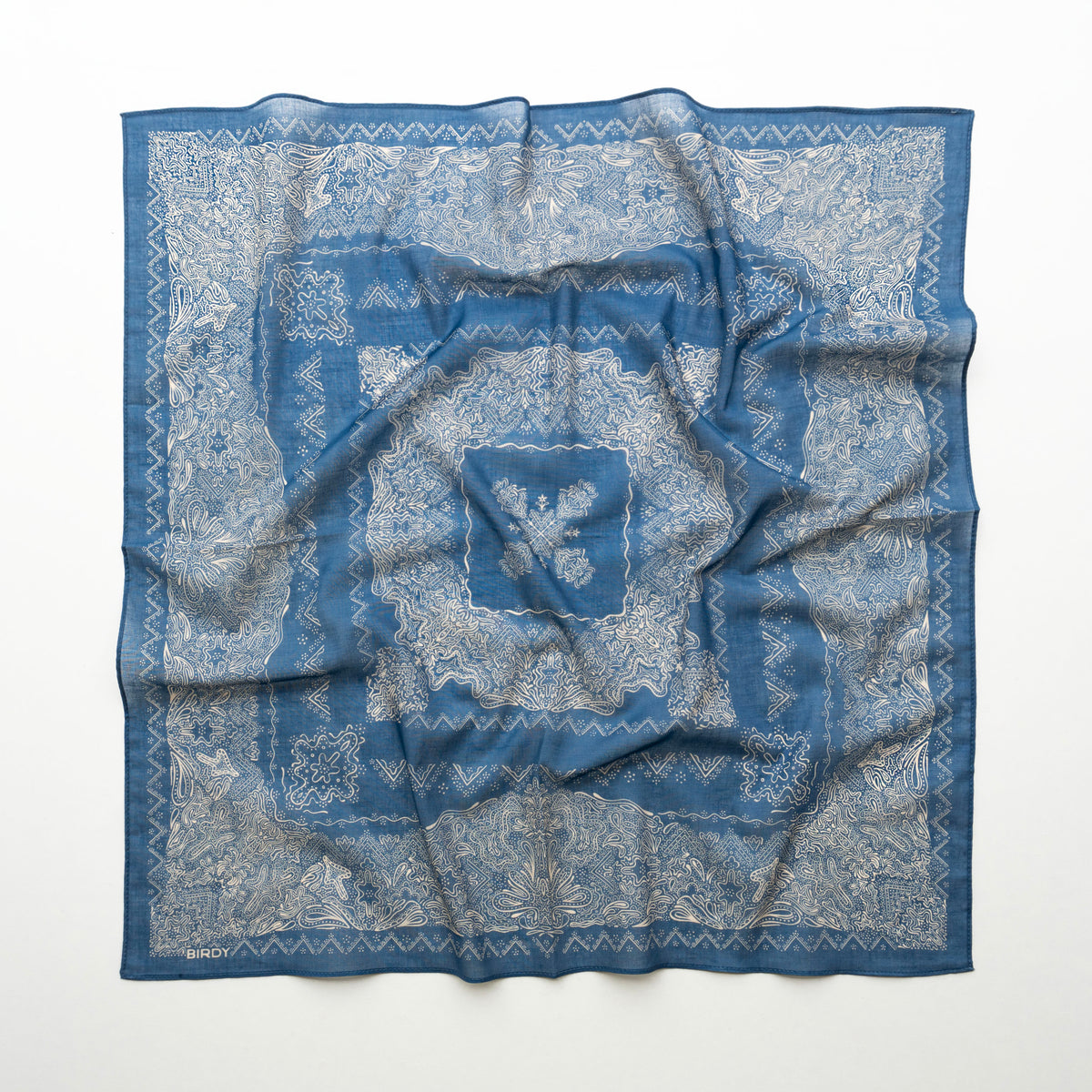 A square blue patterned scarf with a white floral and geometric print, laid flat on a white background.