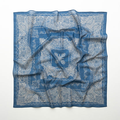 A square blue patterned scarf with a white floral and geometric print, laid flat on a white background.