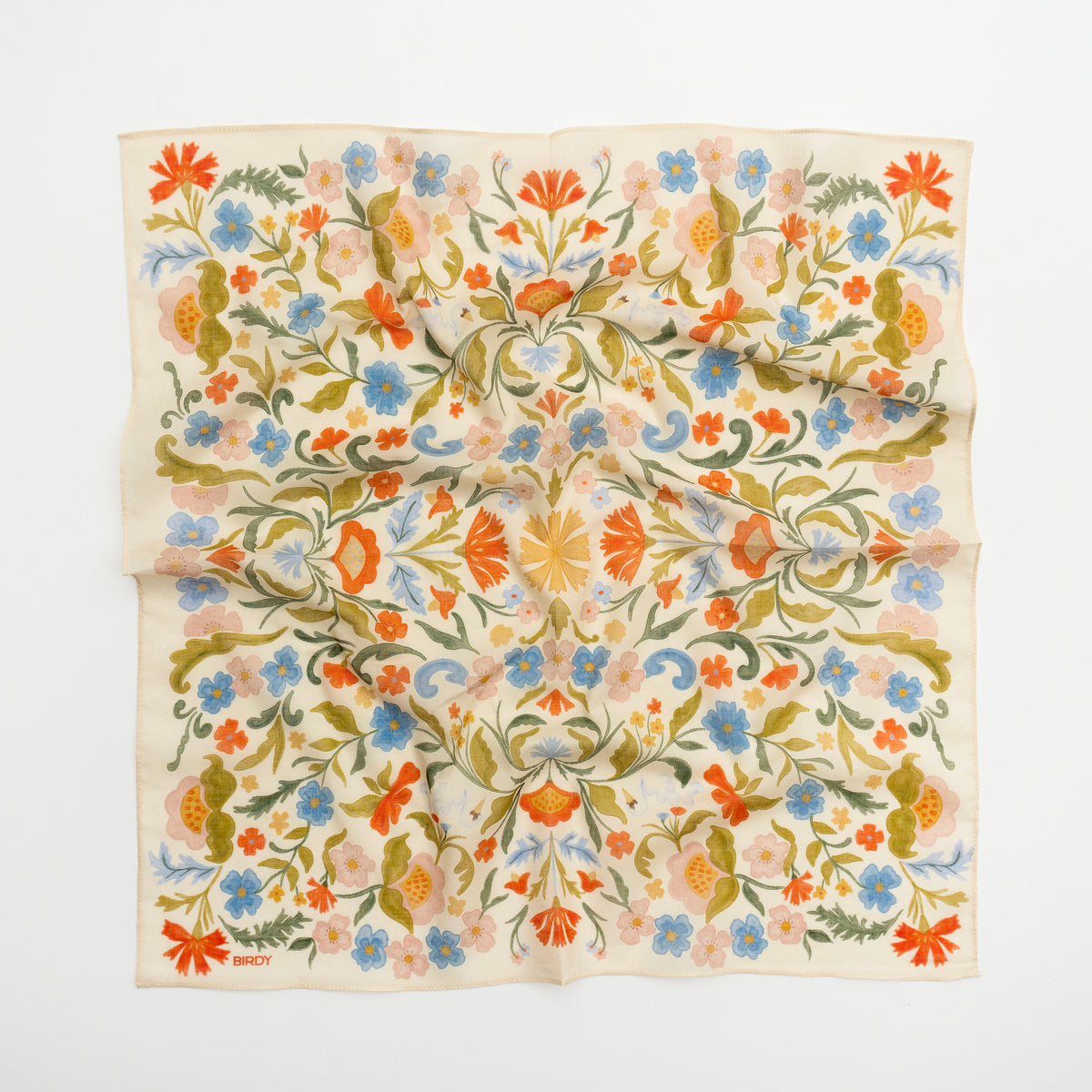 A square cream-colored scarf with an intricate, symmetrical floral pattern in orange, blue, green, and pink, laid flat against a white background.