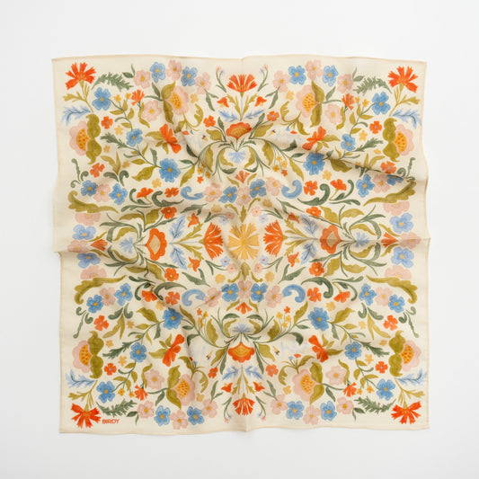 A square cream-colored scarf with an intricate, symmetrical floral pattern in orange, blue, green, and pink, laid flat against a white background.